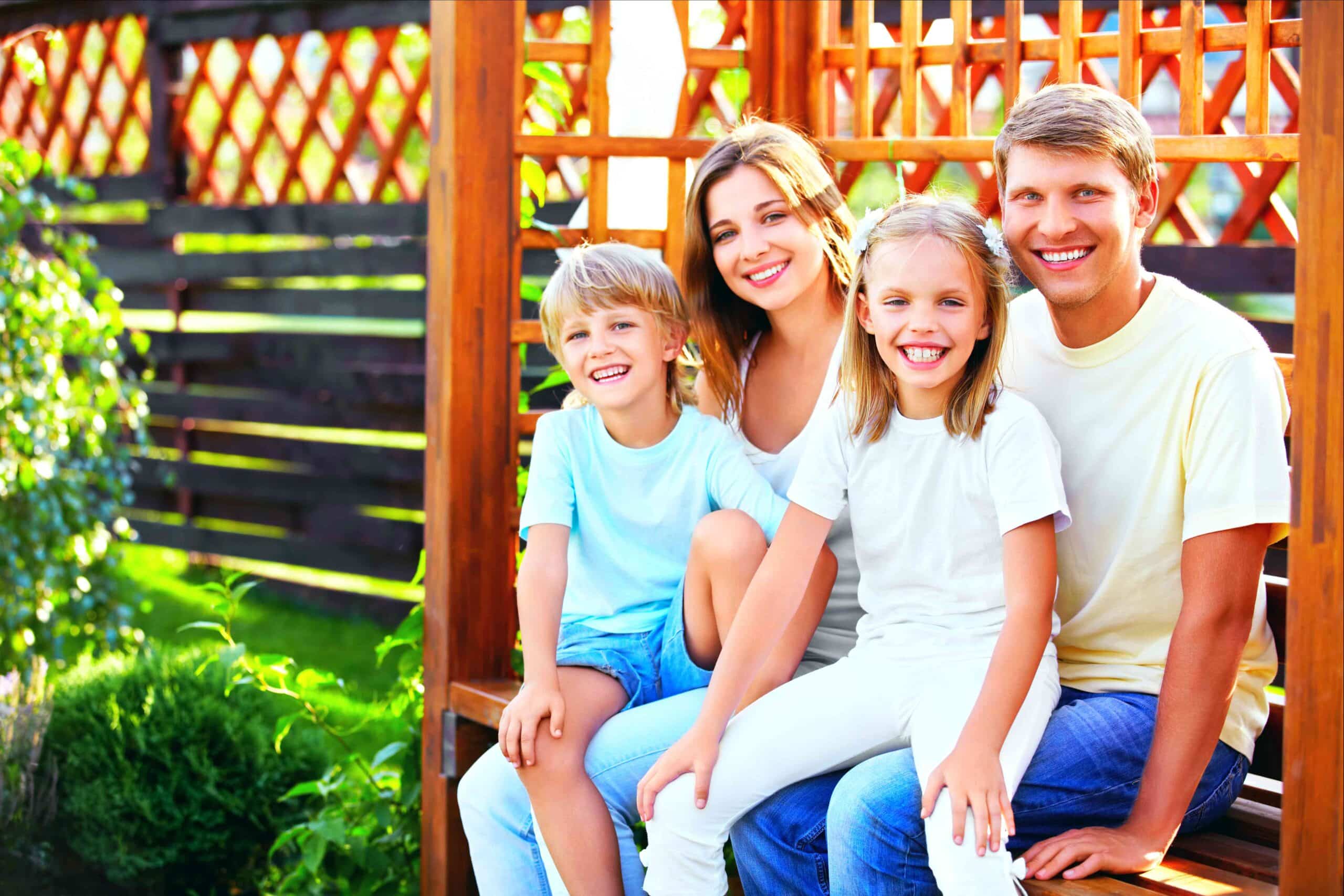 A happy family of four, including parents and two children, standing outdoors in front of a home